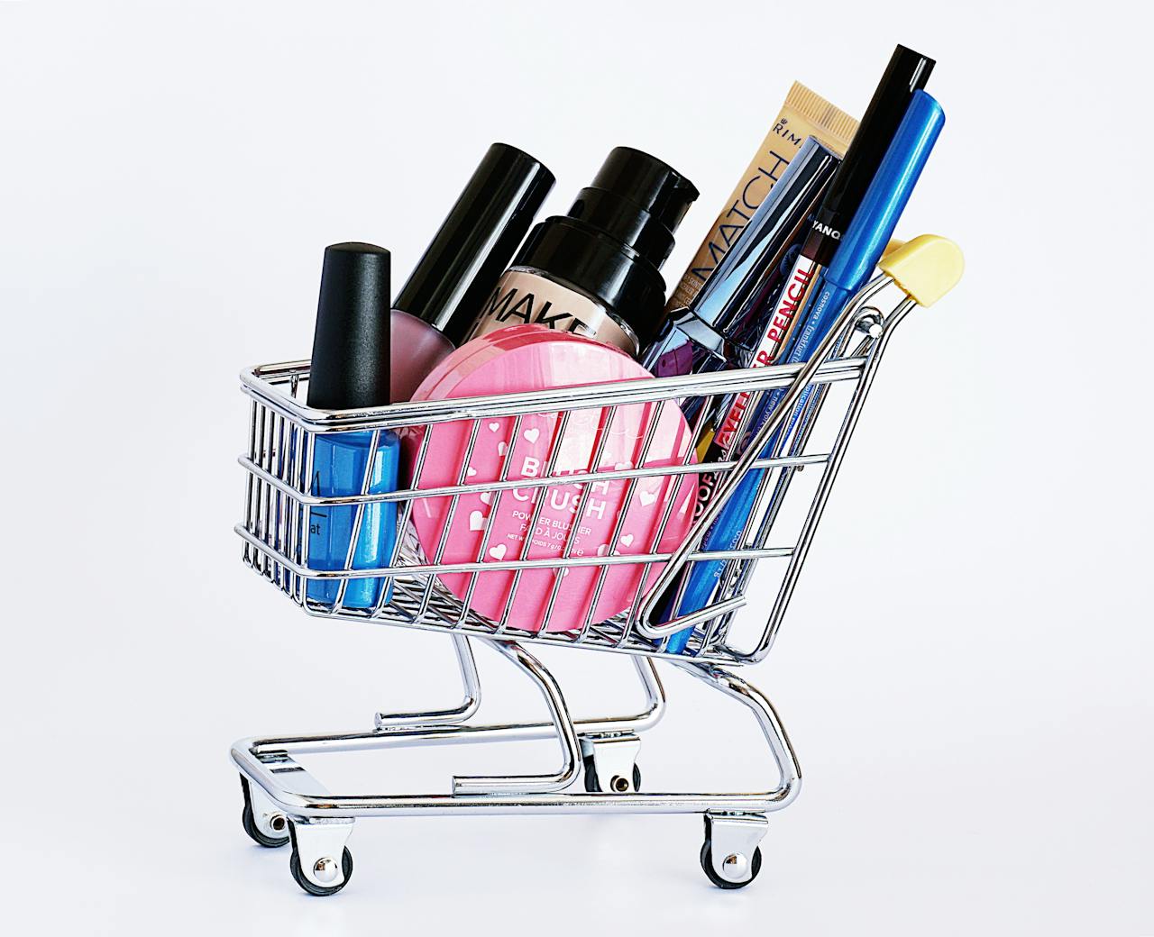 gallery-01 Miniature shopping cart filled with a variety of cosmetics on a white background.